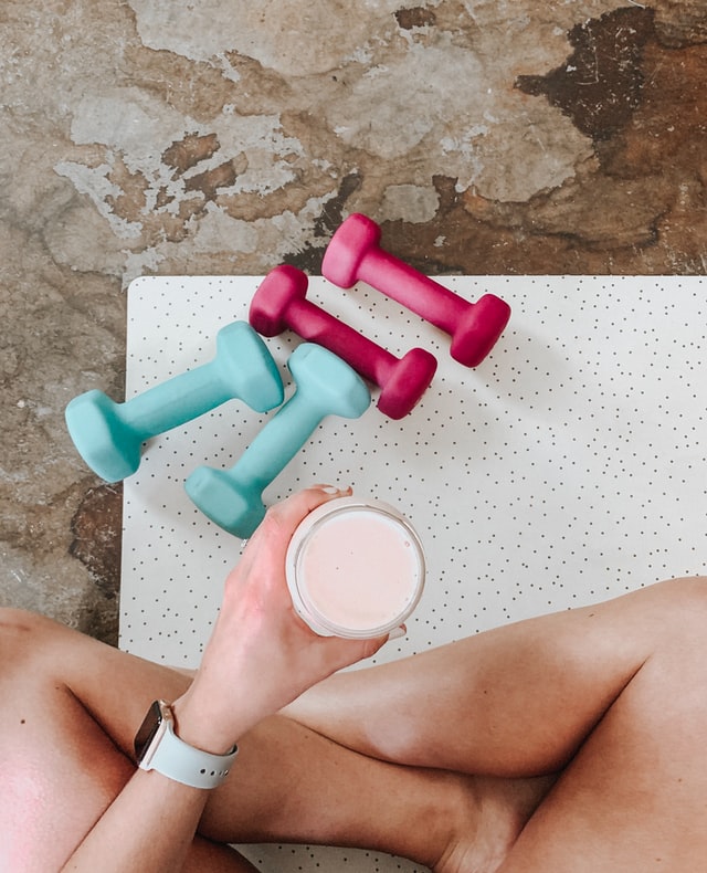 Femme qui tient un verre à la main à côté de deux paires d'haltères